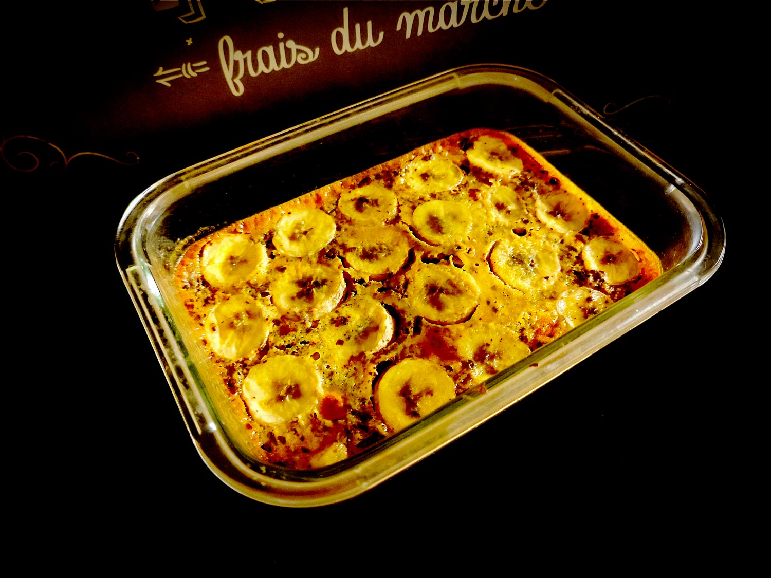 Le clafoutis dans son plat à gratin en verre, qui demande un temps monstrueux à la cuisson. Vraiment, prenez autre chose. On peut voir les tranches de banane disposées sur le dessus du clafoutis, bien caramélisé et craquelé.