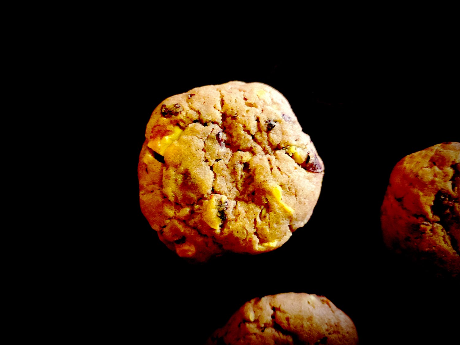 Vu du dessus, un cookie légèrement rose et craquelé duquel on devine les inserts. Au programme, morceaux de myrtilles, de chocolat blanc et de cacahuètes.