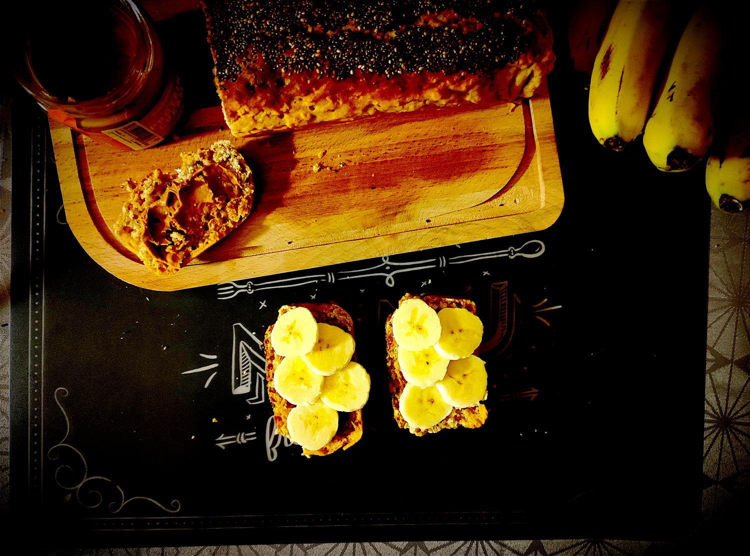 Le pain découpé vu du dessus, bien doré avec ses graines de chia. Sur la première tranche, du beurre de cacahuète. Sur les 2 autres, on est venu y ajouter des tranches de bananes.