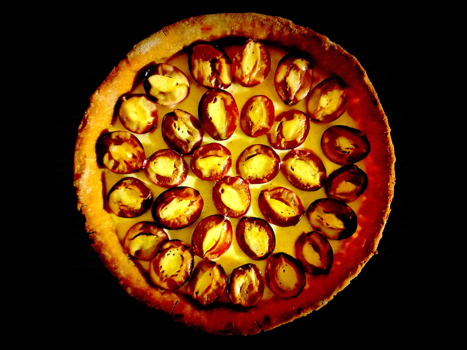 La tarte en entière vue du dessus, avec les quetsches déposées sur l’appareil bien blanc. L’appareil rempli le trou du noyau sur chaque moitié du fruit.