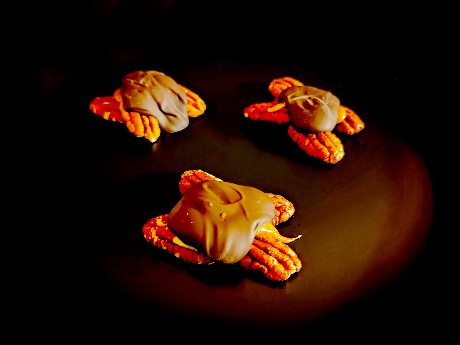 Trois petites tortues vu du dessus. On devine 4 noix de Pécan par tortue, recouvertes de caramel coulant et de chocolat.